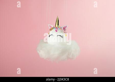 Ostereinhorn-Ei fliegt auf Wolke auf pastellrosa Hintergrund. Frohe ostern Banner. Inspiration für Aktivitäten für Kinder. Grußkarte oder Poster. Speicherplatz kopieren für Stockfoto