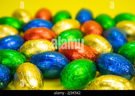 Osterschokolade in bunte Folie eingewickelt. Nahaufnahme auf gelbem Hintergrund Stockfoto