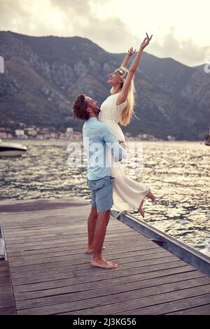 Schöne Hochzeit Foto auf Mountain Lake.Couple verliebt, glückliche Braut in weißem Kleid genießt die Umarmung ihres Mannes Stockfoto