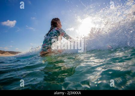 Eine Surferin lässt eine Welle an ihr vorbeiziehen, während sie auf die richtige Welle wartet und sich spritzt. Stockfoto