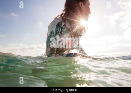 Ein Surfer mit Sonnenschein erwartet für Wellen im klaren, blauen Wasser. Stockfoto