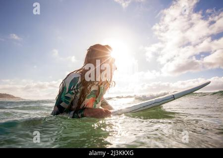 Ein Surfer erwartet Wellen mit Sonnenschein in klaren, blauen Wasser. Stockfoto