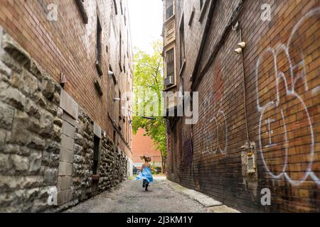 Das junge Mädchen läuft mit Graffiti an Backsteinwänden durch die Gasse; Toronto, Ontario, Kanada Stockfoto