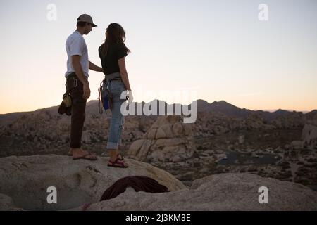 Ein junges Paar nehmen in den Sonnenuntergang nach The Eye Route auf Cyclops Felsen im Joshua Tree National Park zu klettern. Stockfoto