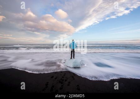 Ein Mann steht auf gewaschen oben Gletschereis auf einem schwarzen Sandstrand. Stockfoto