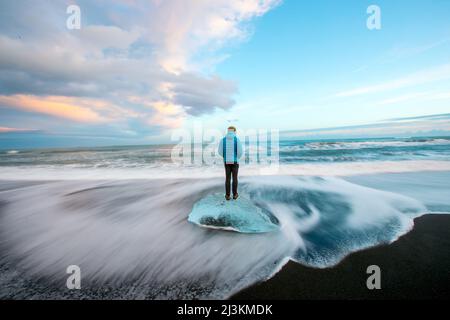 Ein Mann steht auf gewaschen oben Gletschereis auf einem schwarzen Sandstrand. Stockfoto