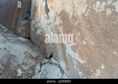 Ein Bergsteiger, der sich eine technische Granitwand hocharbeitet. Stockfoto