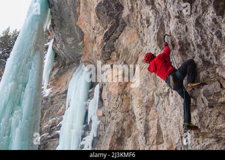 Ein Bergsteiger trocken Werkzeuge eine Felswand mit Eispickel und Steigeisen. Stockfoto