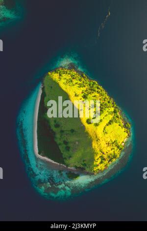 Blick von direkt über eine Insel im Komodo Nationalpark, halb im Sonnenlicht und halb im Schatten, umgeben von türkisfarbenem Wasser des Pazifiks Stockfoto