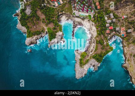 Blick direkt über der felsigen Küste und am Strand des Ferienortes Lembongan mit Gebäuden am Rande des türkisfarbenen Wassers vor ... Stockfoto