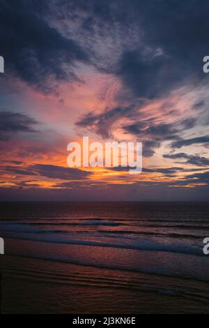 Leuchtender Sonnenuntergang Himmel über dem Ozean mit rosa Sonnenlicht reflektiert auf der Brandung am Ufer des Uluwatu Beach; Badung, Bali, Indonesien Stockfoto