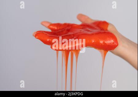 Roter Schleim, der aus der Hand einer Frau auf einem weißen Hintergrund herabfließt. Stockfoto