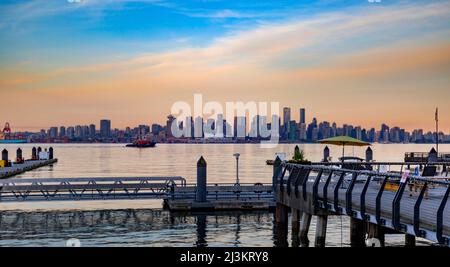 Blick auf die Skyline von Vancouver und die Uferpromenade vom Lonsdale Quay aus, mit Sonnenaufgangsfarben, die sich im Wasser des Burrard Inlet widerspiegeln Stockfoto