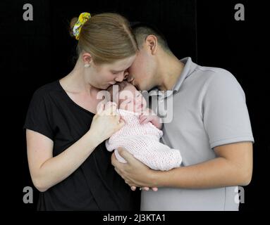 Familienportrait eines jungen Paares mit einem neugeborenen Mädchen vor schwarzem Hintergrund; Studio Stockfoto