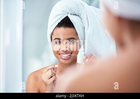 Zahnseide für ein sauberes Lächeln. Aufnahme einer Frau, die ihre Zähne mit einem Handtuch um ihren Kopf gewickelt hat. Stockfoto