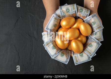 Hand Mann halten goldene Eier und Dollar in einem Korb auf schwarzem Hintergrund, Draufsicht Stockfoto