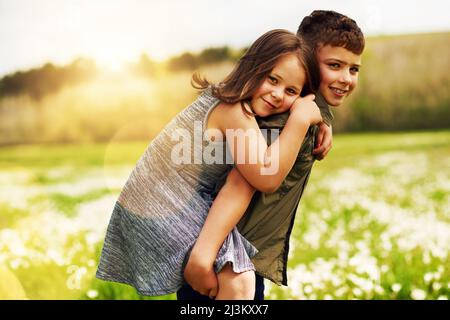 Mein großer Bruder ist mein Held. Porträt eines entzückenden kleinen Jungen, der seiner kleinen Schwester eine Huckepack-Fahrt draußen gab. Stockfoto