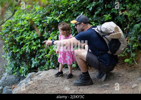 Vater und seine junge Tochter machen eine Pause, um die Natur zu erkunden, Smuggler Cove Marine Provincial Park, Sunshine Coast, BC, Kanada; British Columbia, Kanada Stockfoto