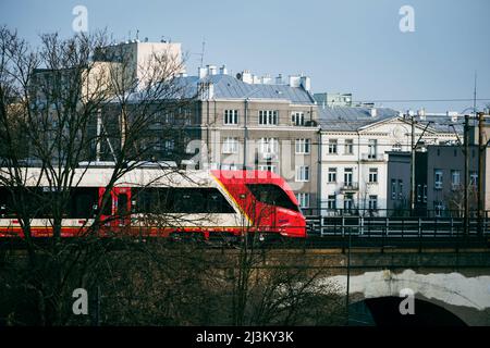 Warschau. Polen. 03.30.2022. Ein moderner Zug fährt über die Brücke auf dem Hintergrund von Stadtgebäuden. Stockfoto