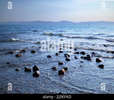 Sonnenlicht erhellt die Felsen im seichten Wasser der Ebbe, während die Brandung in Davis Bay, Sunshine Coast, BC, Kanada, zum Ufer einspült Stockfoto