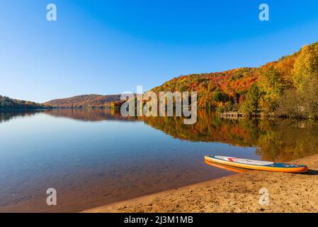 Lake Tremblant und Herbstfarben entlang der Küste mit einem Paddelbrett am Strand; Mont-Tremblant, Quebec, Kanada Stockfoto