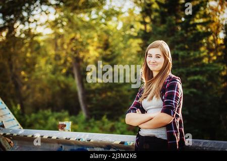Das Teenager-Mädchen steht im Freien mit gekreuzten Armen und blickt auf die Kamera; Edmonton, Alberta, Kanada Stockfoto