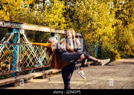 Zwei Schwestern, die im Herbst in einem Park zusammen dumm sind, eine Schwester trägt die andere; Edmonton, Alberta, Kanada Stockfoto