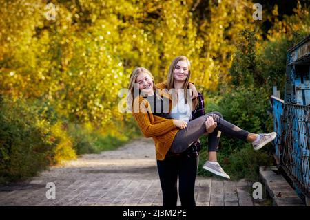 Zwei Schwestern, die im Herbst in einem Park zusammen dumm sind, eine Schwester trägt die andere; Edmonton, Alberta, Kanada Stockfoto