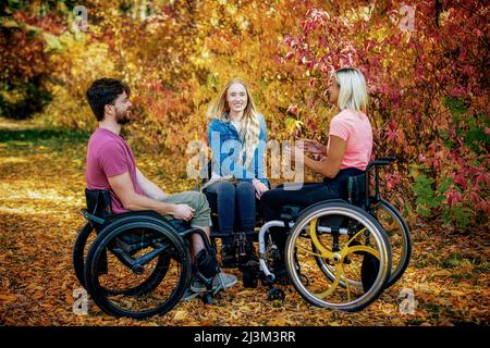 Eine Gruppe von drei jungen Querschnittsgelähmten, die an einem schönen Herbsttag gemeinsam in einem Park in Edmonton, Alberta, Kanada, unterwegs waren Stockfoto