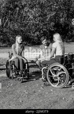 Schwarz-Weiß-Bild einer Gruppe von drei jungen Querschnittsgelähmten in ihren Rollstühlen, die an einem schönen sonnigen Tag gemeinsam in einem Park zu Besuch sind Stockfoto