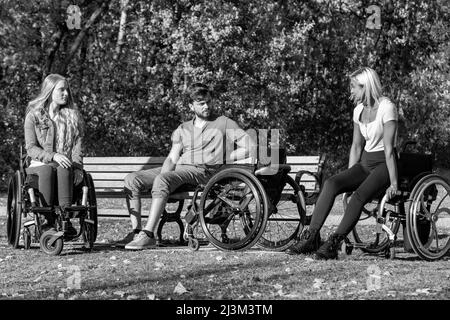 Schwarz-Weiß-Bild einer Gruppe von drei jungen Querschnittsgelähmten in ihren Rollstühlen, die an einem schönen sonnigen Tag gemeinsam in einem Park zu Besuch sind Stockfoto