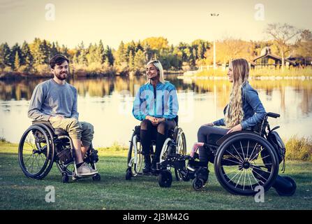 Eine Gruppe von drei jungen Querschnittsgelähmten, die an einem schönen Herbsttag gemeinsam in einem Park in Edmonton, Alberta, Kanada, unterwegs waren Stockfoto