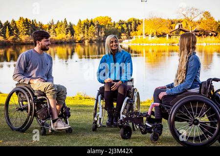 Eine Gruppe von drei jungen Querschnittsgelähmten, die an einem schönen Herbsttag gemeinsam in einem Park in Edmonton, Alberta, Kanada, unterwegs waren Stockfoto