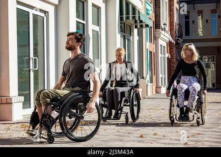 Drei junge querschnittsgelähmte Freunde verbringen Zeit miteinander, um einen Gehweg außerhalb eines Stadtgebiets zu befahren; Edmonton, Alberta, Kanada Stockfoto