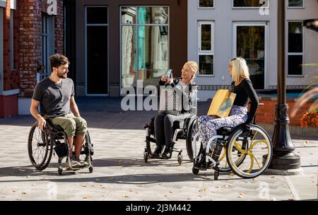 Drei junge querschnittsgelähmte Freunde verbringen Zeit miteinander, um draußen in einem Stadtgebiet zu shoppen und Fotos zu machen; Edmonton, Alberta, Kanada Stockfoto