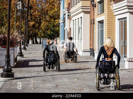 Drei junge querschnittsgelähmte Freunde verbringen Zeit miteinander, um einen Gehweg außerhalb eines Stadtgebiets zu befahren; Edmonton, Alberta, Kanada Stockfoto