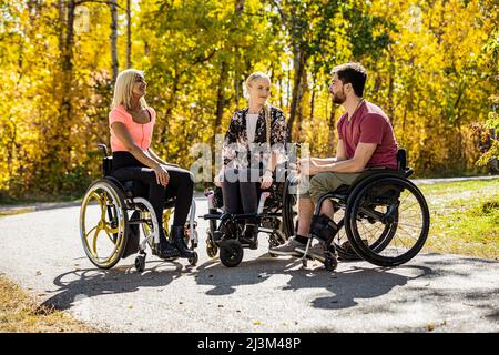 Eine Gruppe von drei jungen Querschnittsgelähmten, die an einem schönen Herbsttag gemeinsam in einem Park in Edmonton, Alberta, Kanada, unterwegs waren Stockfoto