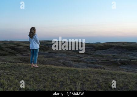 Frau, die den Sonnenuntergang über den Prärien von Saskatchewan im Grasslands National Park, Saskatchewan, Kanada, betrachtet Stockfoto