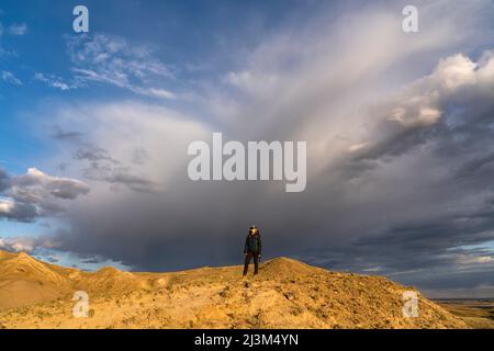 Dramatische Wolkenbildung am Himmel hinter einer Frau auf einem Bergrücken im Grasslands National Park, Saskatchewan, Kanada; Val Marie, Saskatchewan, Kanada Stockfoto