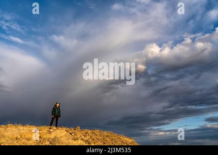 Dramatische Wolkenbildung am Himmel hinter einer Frau auf einem Bergrücken im Grasslands National Park, Saskatchewan, Kanada; Val Marie, Saskatchewan, Kanada Stockfoto