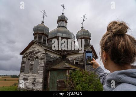 Frau, die mit ihrem Smartphone Fotos von einer alten Kirche im ländlichen Saskatchewan macht; Maryville, Saskatchewan, Kanada Stockfoto