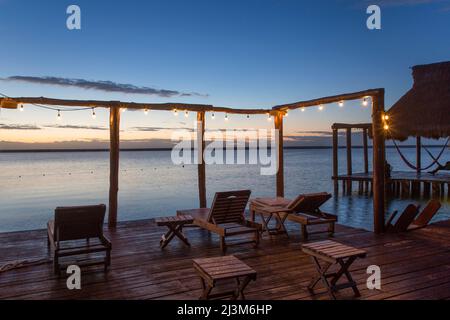 Dock mit Sitzgelegenheiten und einer Reihe von beleuchteten Lichtern am Wasser im Rancho Encantado Eco-Resort & Spa; Bacalar, Quintana Roo, Mexiko Stockfoto