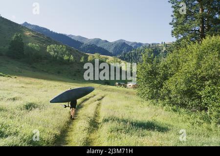 Eine Frau trägt ein Kajak in der Nähe der Mittelgabel des Salmon River.; Salmon River, Idaho. Stockfoto