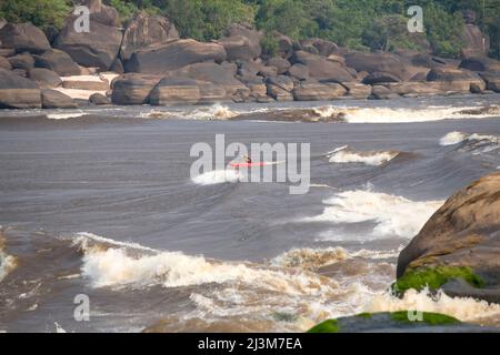 Ein Kajakfahrer paddelt durch einen Wellenzug, der sich einer anderen Geschwindigkeit nähert.; Unterer Kongo-Fluss, Demokratische Republik Kongo. Stockfoto