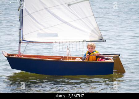 Ein achtjähriger Junge, der ein kleines Boot im Sommersegelcamp segelt, das vom Roanoke Island Maritime Museum in Manteo, North Carolina, betrieben wird. Stockfoto