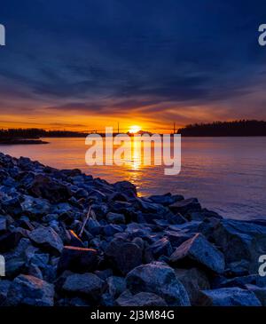 Brillante Farben eines Sonnenaufgangs, der von der Ufermauer in West Vancouver aus gesehen wird, mit Blick auf die Lions Gate Bridge in der Ferne Stockfoto