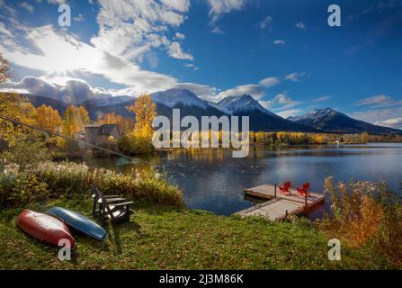 Zwei rote Stühle auf einer Terrasse auf dem ruhigen See Kathlyn, umgeben von herbstbunten Bäumen und schneebedeckten Coast Mountains, vom Lakedrop Inn, Wa... Stockfoto