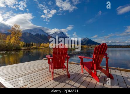 Zwei rote Stühle auf einer Terrasse auf dem ruhigen See Kathlyn, umgeben von herbstbunten Bäumen und schneebedeckten Coast Mountains, vom Lakedrop Inn, Wa... Stockfoto