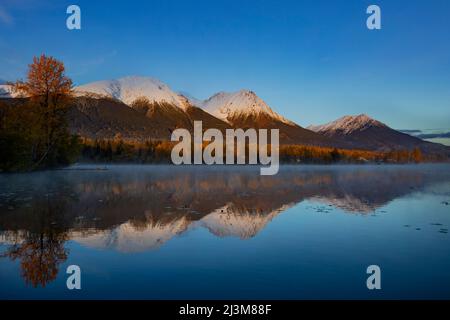 Beschaulicher See Kathlyn, umgeben von herbstlichen Bäumen und schneebedeckten Coast Mountains, vom Lakedrop Inn, Watson's Landing, BC, Kanada aus gesehen Stockfoto