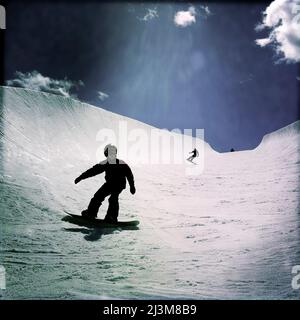 Ein elfjähriger Junge und seine Mutter Snowboarden in einer großen Halfpipe.; Winter Park, Colorado. Stockfoto